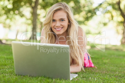 Peaceful attractive woman using her notebook lying on a lawn