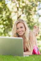 Cute woman using her notebook lying on a lawn