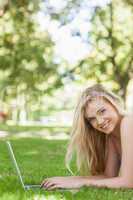 Portrait of cheerful young woman using her notebook lying on a l