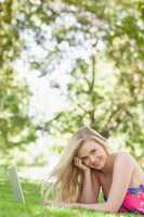 Portrait of cheerful attractive woman lying on a lawn using her