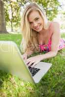 Cheerful young woman working with her notebook lying in a park