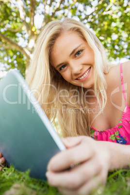 Calm attractive woman holding her tablet lying on a lawn