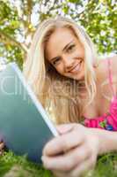 Calm attractive woman holding her tablet lying on a lawn