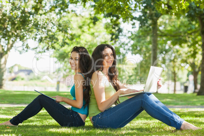 Two cute brunette women sitting on a lawn smiling at camera