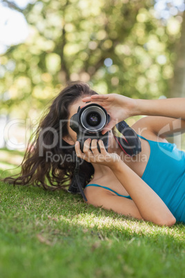 Young brunette woman lying on a lawn taking a picture