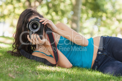 Front view of pretty brunette woman lying on a lawn taking a pic