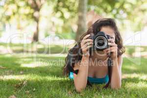 Front view of brunette woman lying on a lawn for taking a pictur