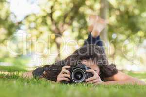 Young woman using her camera for taking a picture lying on a law
