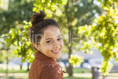 Cute brunette woman wearing a brown coat posing in a park