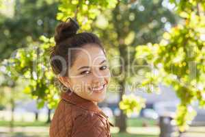 Cute brunette woman wearing a brown coat posing in a park