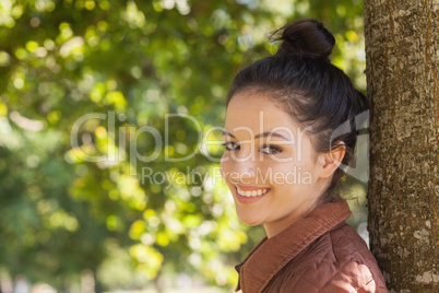 Beautiful young woman posing leaning against a tree