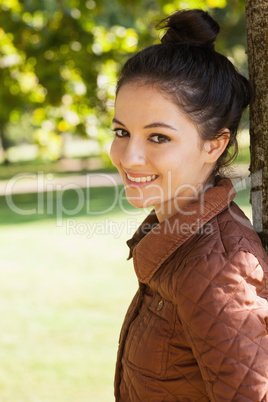 Side view of lovely woman leaning against a tree