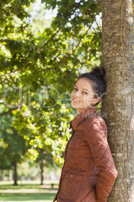 Side view of attractive brunette woman leaning against a tree
