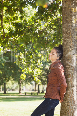 Attractive woman leaning against a tree with closed eyes