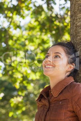 Side view of cheerful young woman leaning against a tree