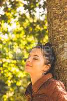 Side view of brunette woman leaning against a tree