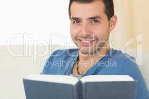 Casual smiling man sitting on couch holding a book