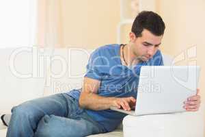 Casual calm man sitting on couch using laptop