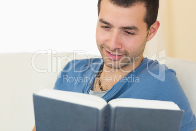 Casual smiling man sitting on couch reading a book