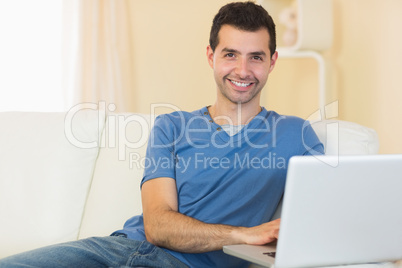 Casual smiling man sitting on couch using laptop