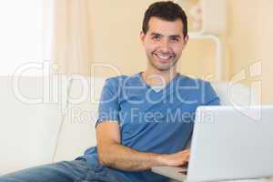 Casual smiling man sitting on couch using laptop