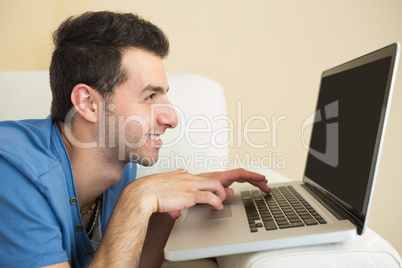 Casual smiling man sitting on couch using and looking at laptop