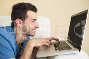 Casual smiling man sitting on couch using and looking at laptop