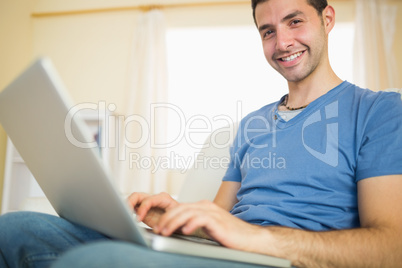 Casual attractive man sitting on couch using laptop looking at c