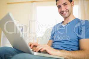 Casual attractive man sitting on couch using laptop looking at c