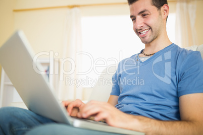 Casual attractive man sitting on couch using looking at laptop