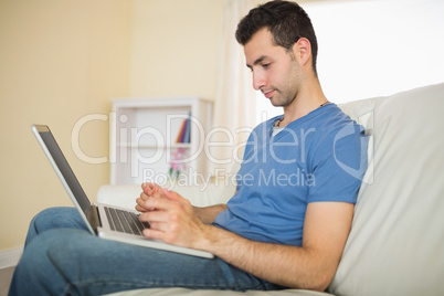 Casual calm man sitting on couch using looking at laptop