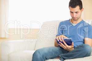 Casual calm man using tablet sitting on couch