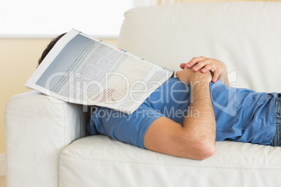 Casual man lying on couch with newspaper covering head