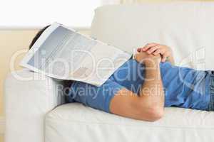 Casual man lying on couch with newspaper covering head