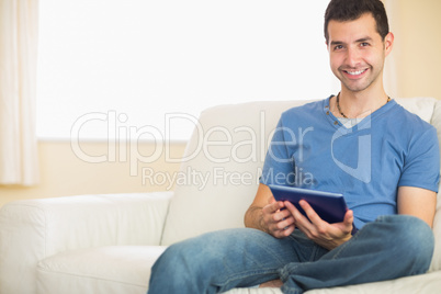 Casual smiling man using tablet sitting on couch