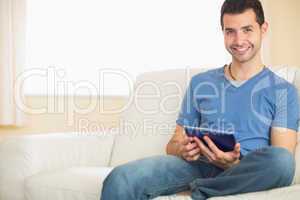 Casual smiling man using tablet sitting on couch