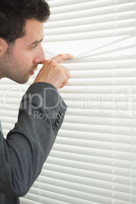 Handsome serious businessman spying through roller blind