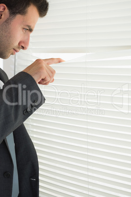 Handsome frowning businessman spying through roller blind