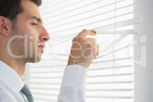 Attractive frowning businessman spying through roller blind