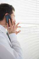 Attractive businessman spying through roller blind while phoning