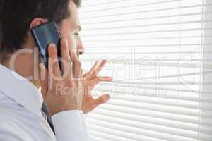 Handsome businessman spying through roller blind while phoning