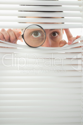 Male eyes spying through roller blind with magnifier