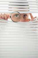 Male eyes spying through roller blind with magnifier