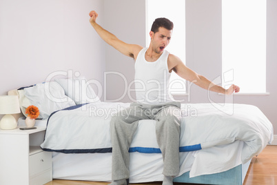 Yawning casual man sitting on bed stretching his arms