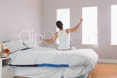 Rear view of man sitting on bed stretching his arms