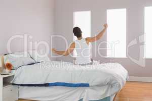 Rear view of man sitting on bed stretching his arms