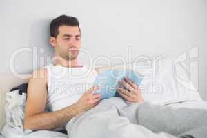 Handsome calm man reading book in his bed