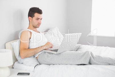 Handsome calm man using laptop in his bed