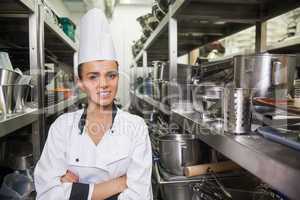 Young cheerful chef standing arms crossed between shelves