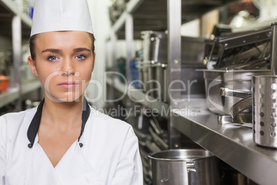 Young unsmiling chef standing arms crossed between shelves